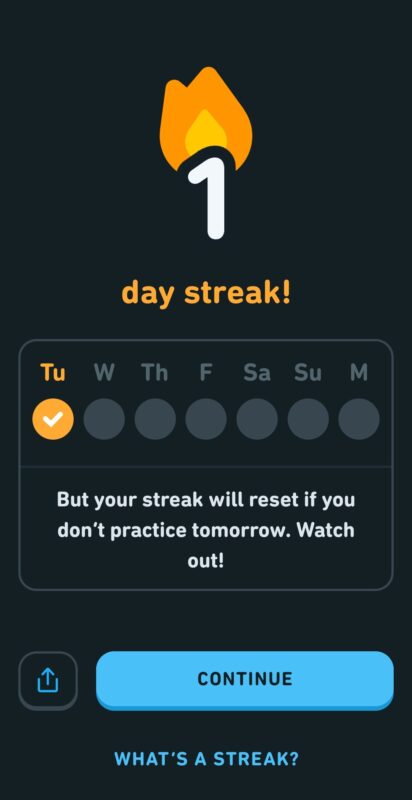 Скриншот экрана в приложении Duolingo. Вверху экрана есть текст: 1 день подряд. Ниже находится недельный календарь с отмеченным вторником. Под календарем находится текст: «Но ваша серия обнуляется, если вы не будете тренироваться завтра». Осторожно! Внизу экрана есть синяя кнопка с надписью «Продолжить». Под синей кнопкой находится текст: Что такое полоса?
