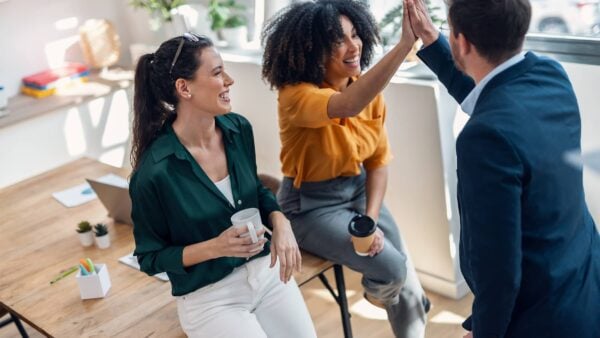 three happy people drinking coffee and talking in an office environment