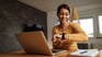 woman brown shirt table laptop looking at smartwatch